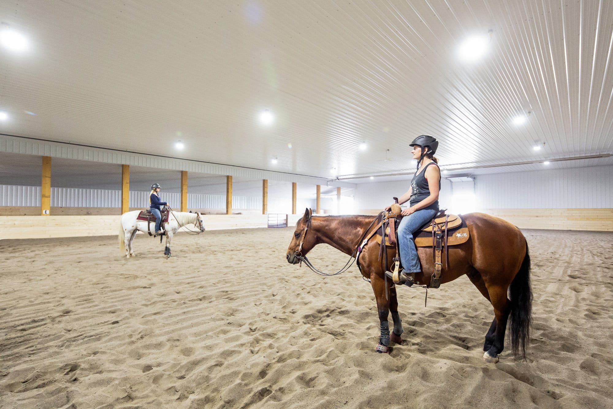 Riders sit on top of horses in a fully finished indoor riding arena.