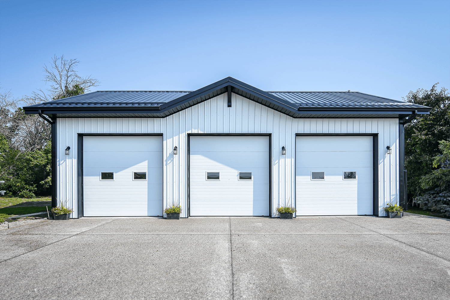 Post frame building with three garages bays, a white exterior and black roof