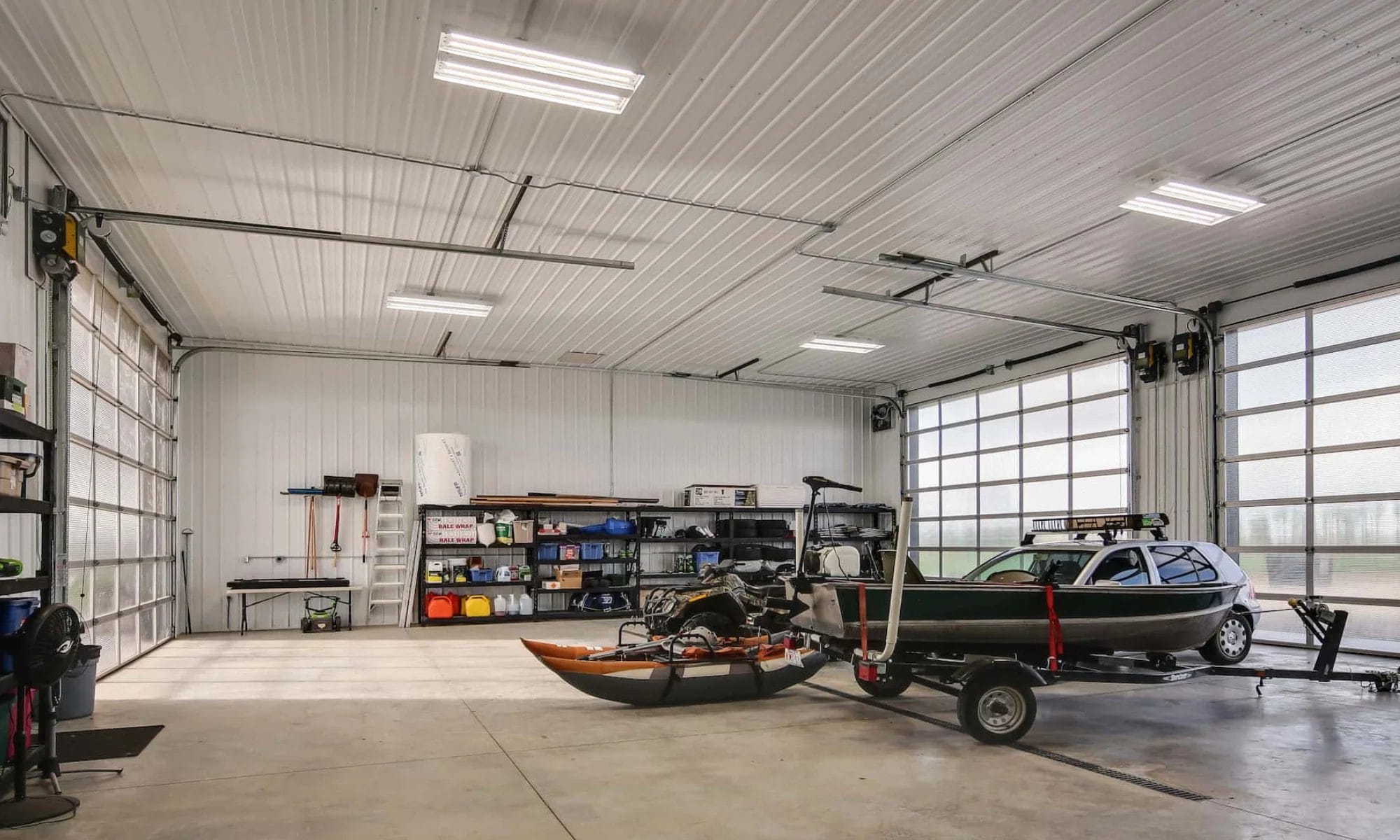 Interior of a pole barn building garage with storage capacity for a boat and other vehicles, brightly lit by an overhead door with glass panels.