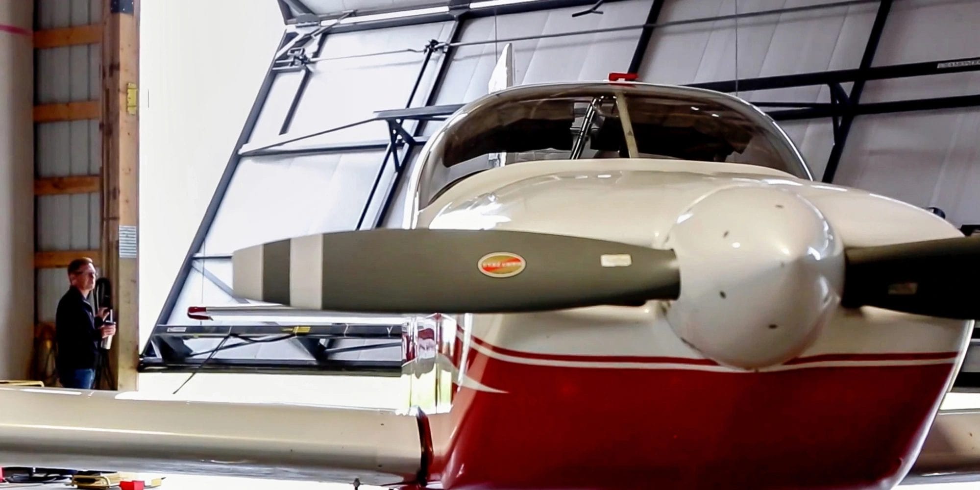 Red and white airplane sitting inside a post frame hangar. The polit opens the door in the background