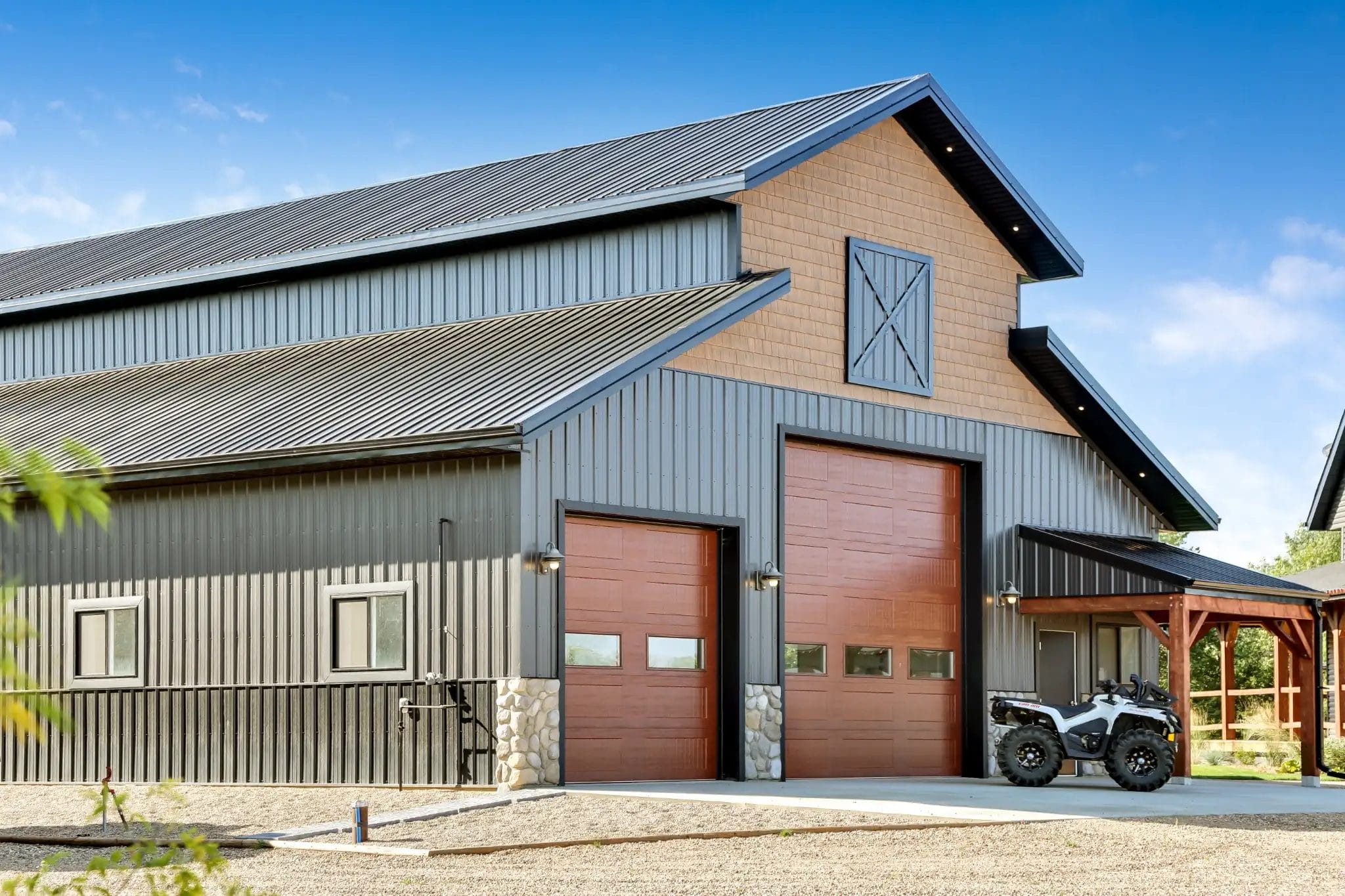 Stone wainscoting, a faux hay door, and a porch combine to create a polished appearance on a monitor-style workshop for an upscale acreage.