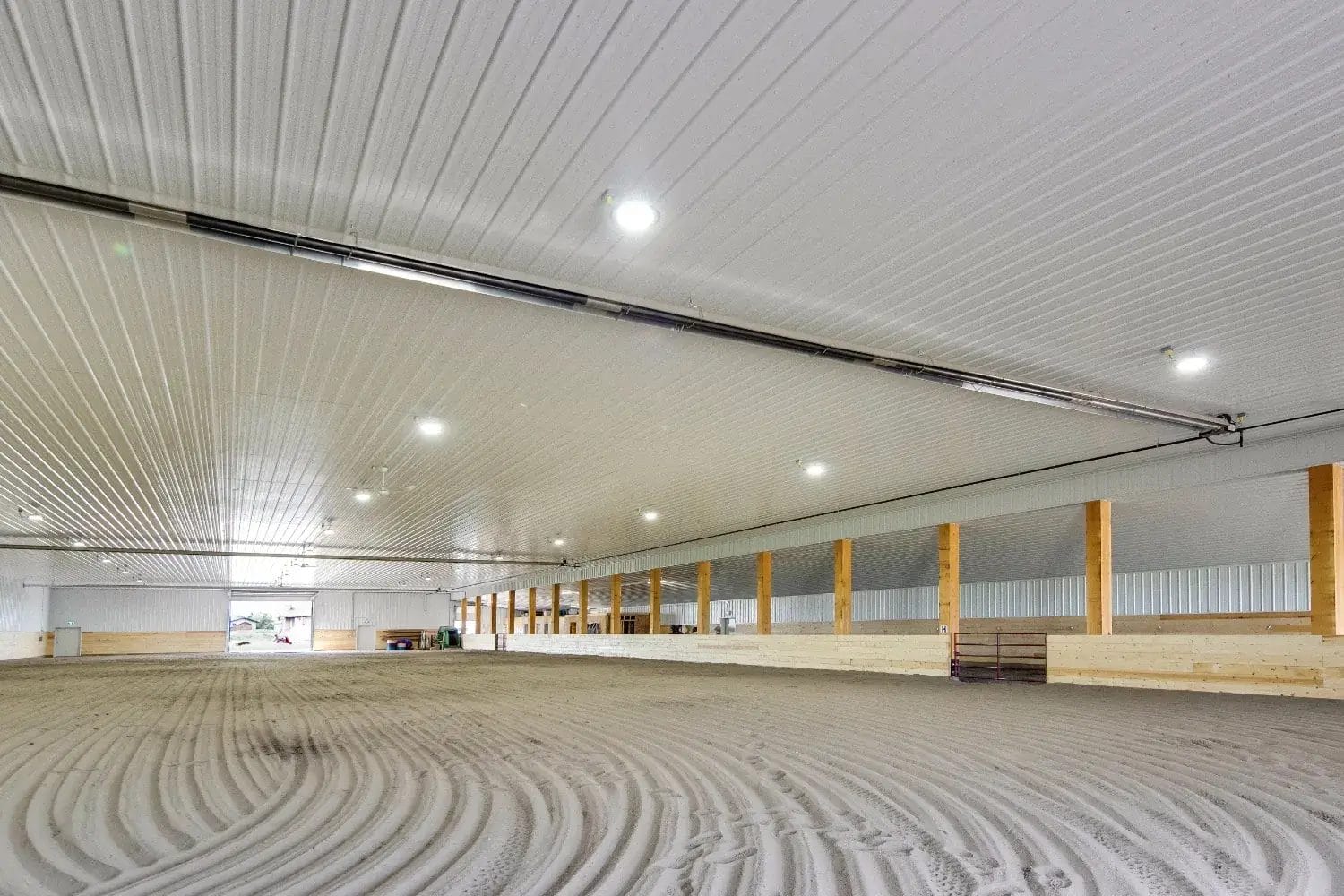 A clear-span indoor riding arena constructed using post frame methods sits empty awaiting riders and horses.
