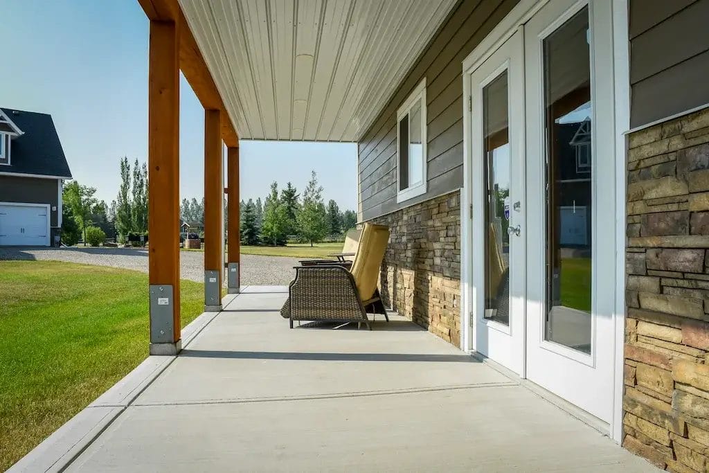 Stone wainscoting runs along the side of a post frame garage underneath a porch