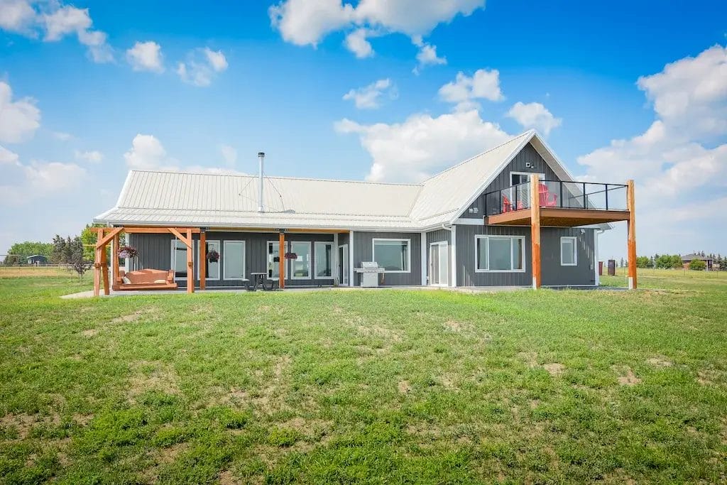 The rear elevation of a post frame shop home with covered porch and second floor deck overlooking the countryside
