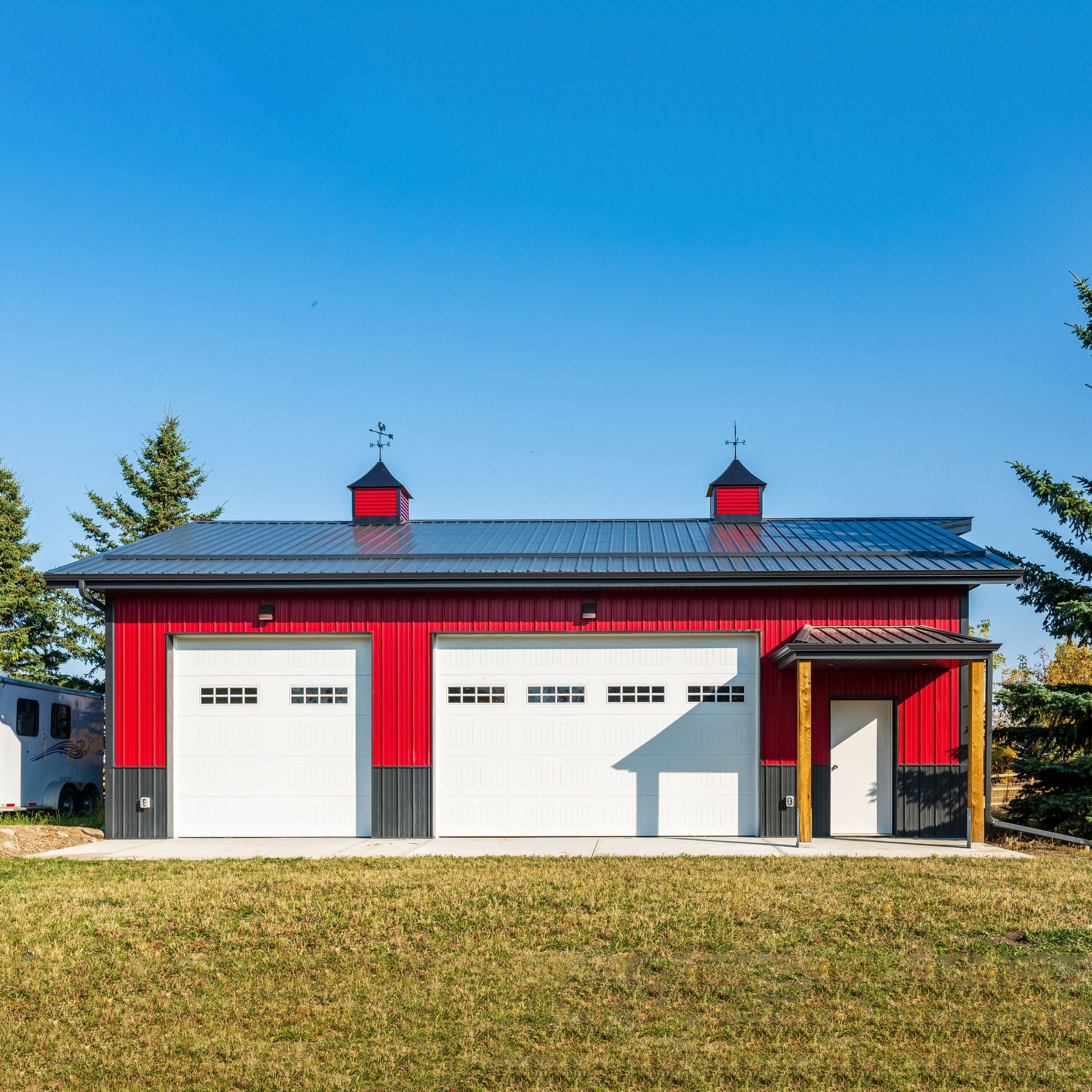 A wide angle picture shows a highly custom and attention-grabbing post frame acreage outbuilding with red and whit metal