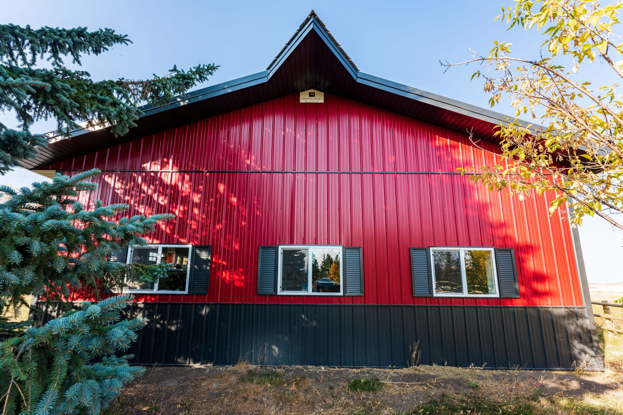 A red and black acreage outbuilding proudly showcases premium custom details like wainscoting, faux shutters and a widow's peak detail