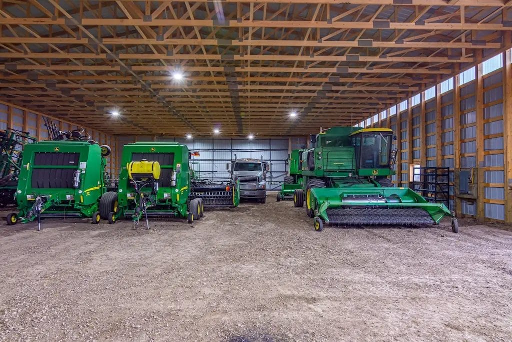 John Deere combines and implements inside a post frame machine shed
