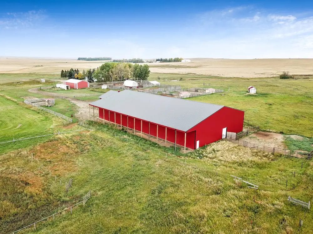 Red post frame riding arena with a full-length lean-to for hay storage