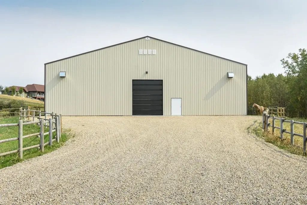 Exterior of post frame riding arena with horse stalls at the end of a driveway
