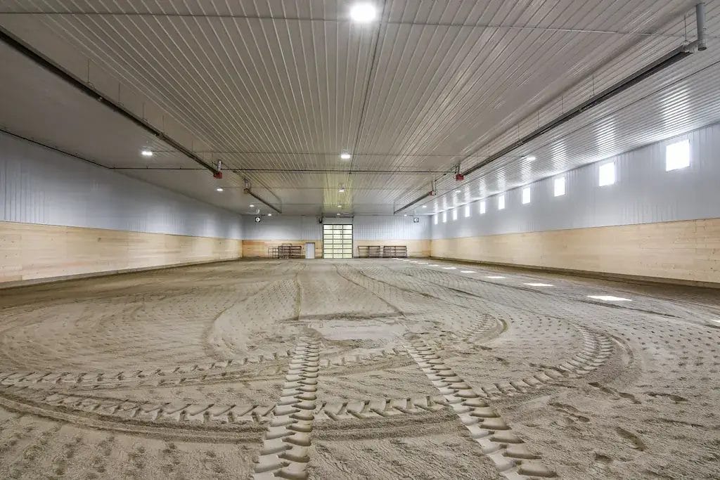 Pole barn indoor riding arena interior is brightly lit with windows and kick wall