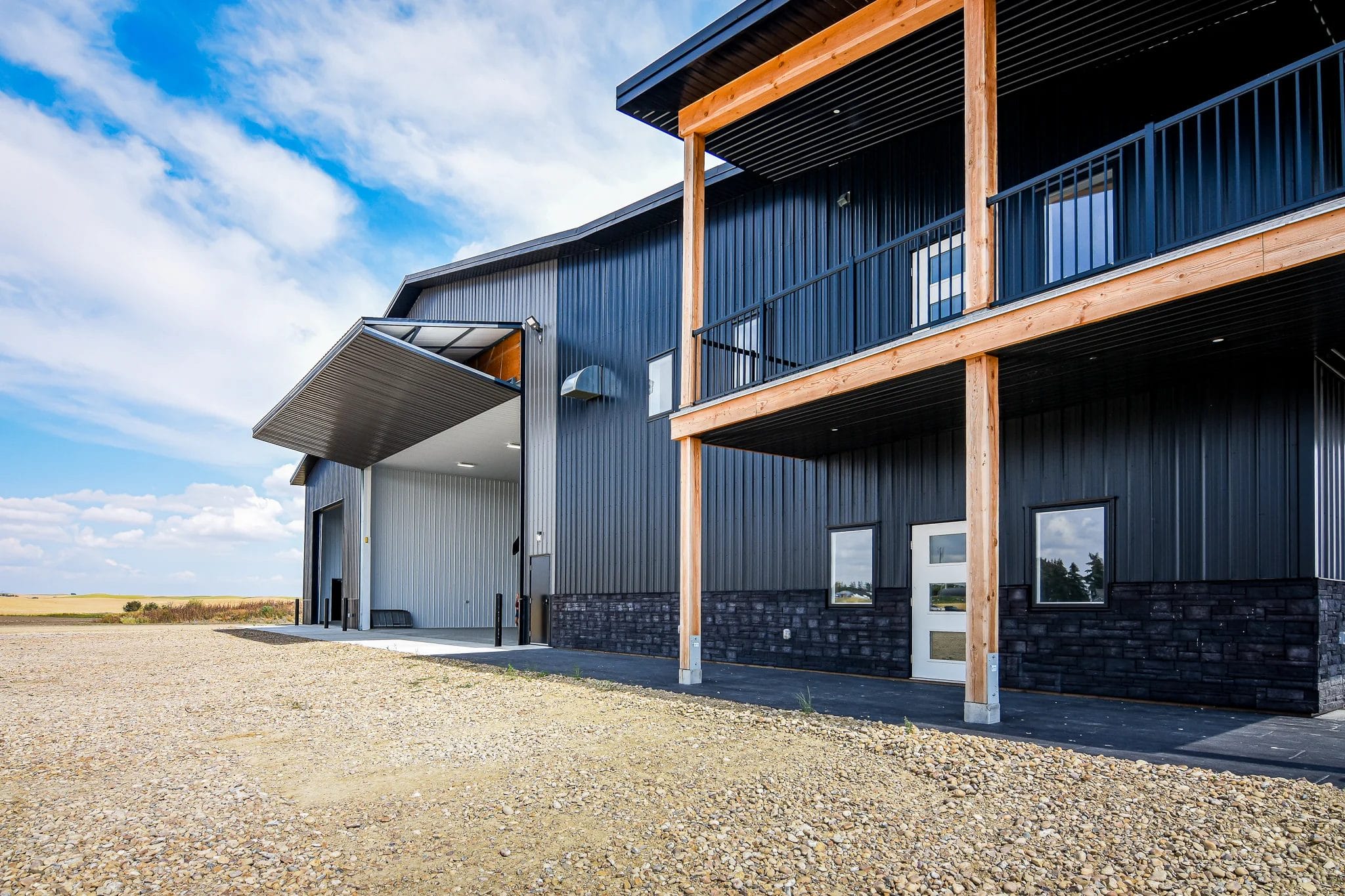 Modern post frame building with black metal siding, upper balcony, and large overhead doors built by professional post frame builders.