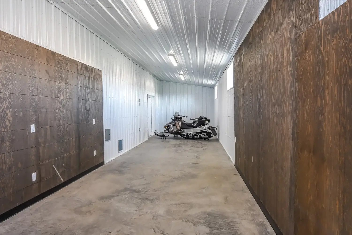 The enclosed lean-to of a post frame acreage shop houses a snowmobile.