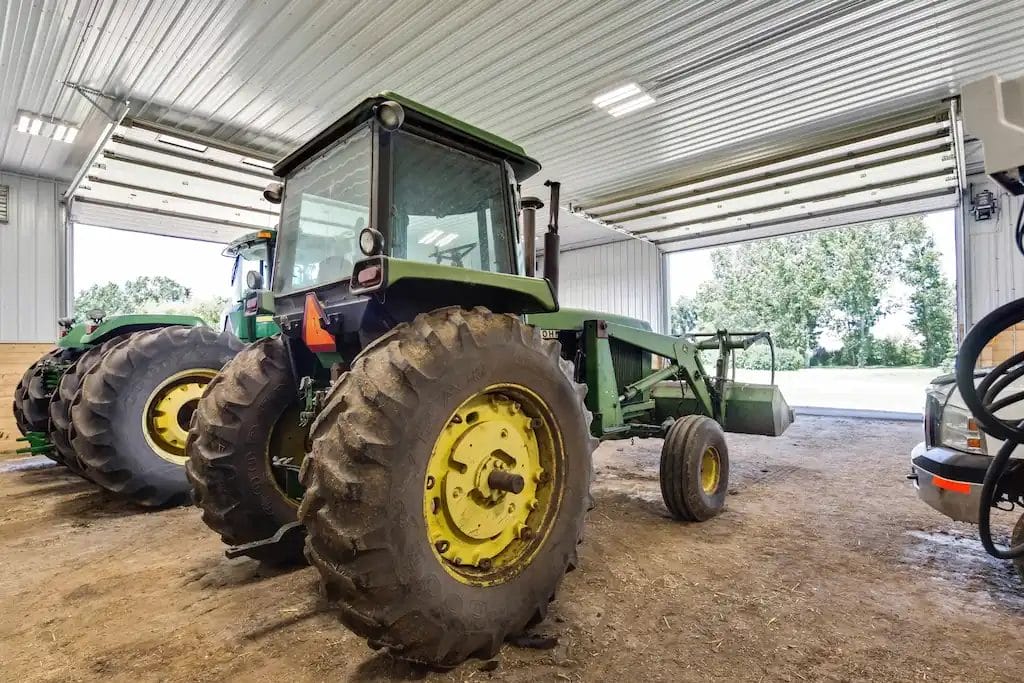 Tractors and other farm equipment sit inside a post frame cattle barn.