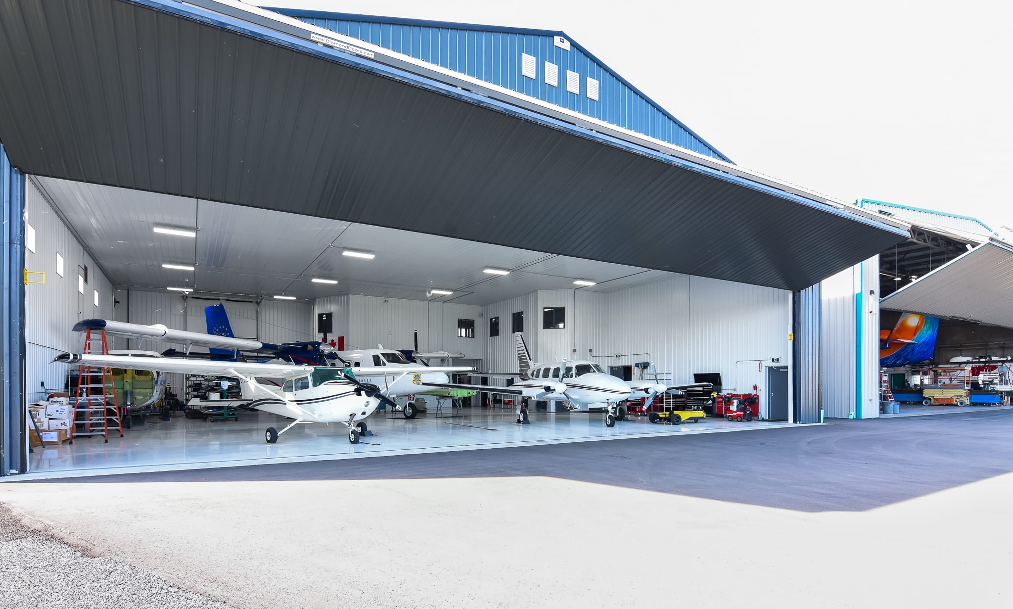 Aircraft hangar with blue exterior and large bi-fold doors that are open, showing aircrafts within.