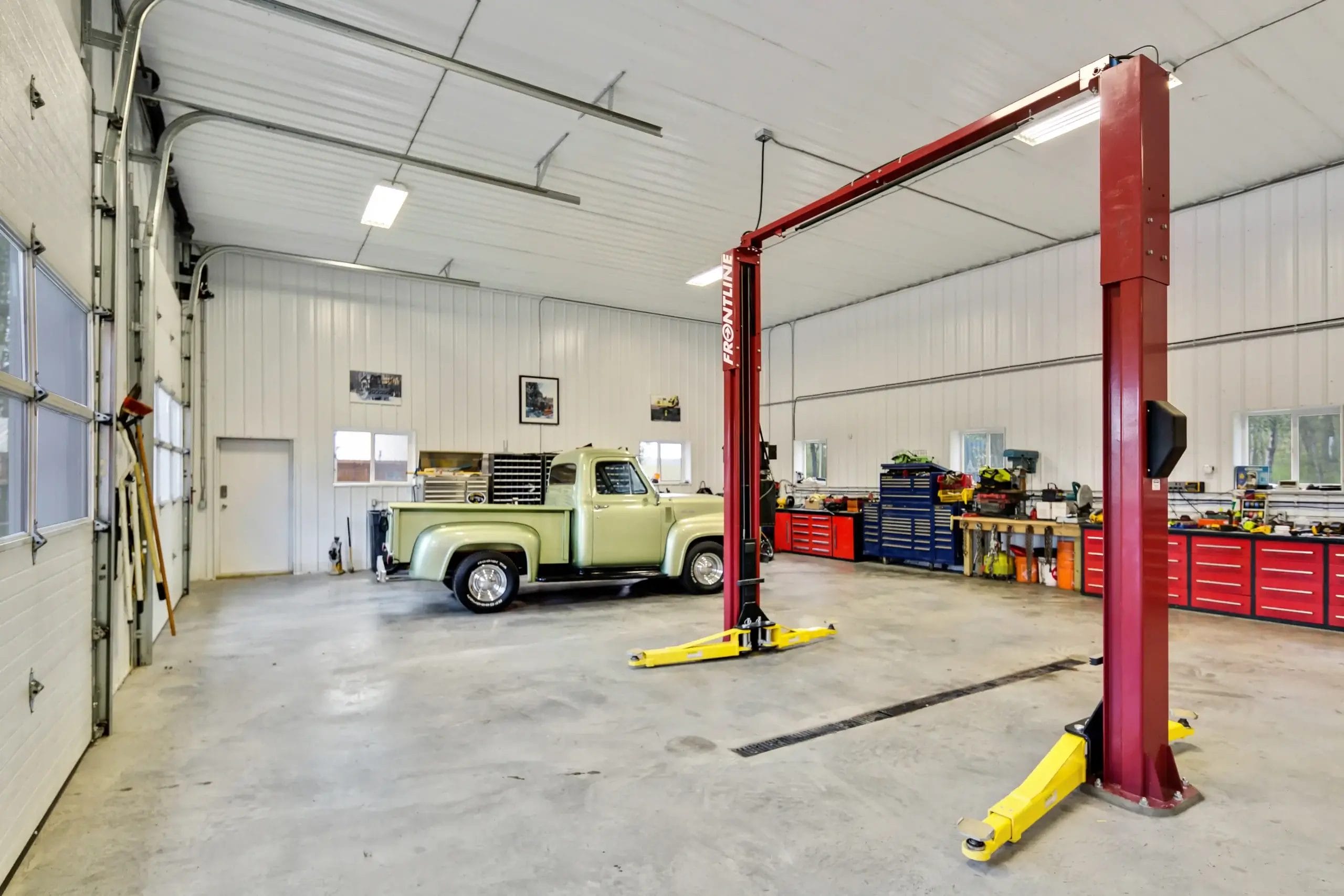 Brightly lit interior of an insulated post frame garage with work benches, tool boxes, and a car lift.