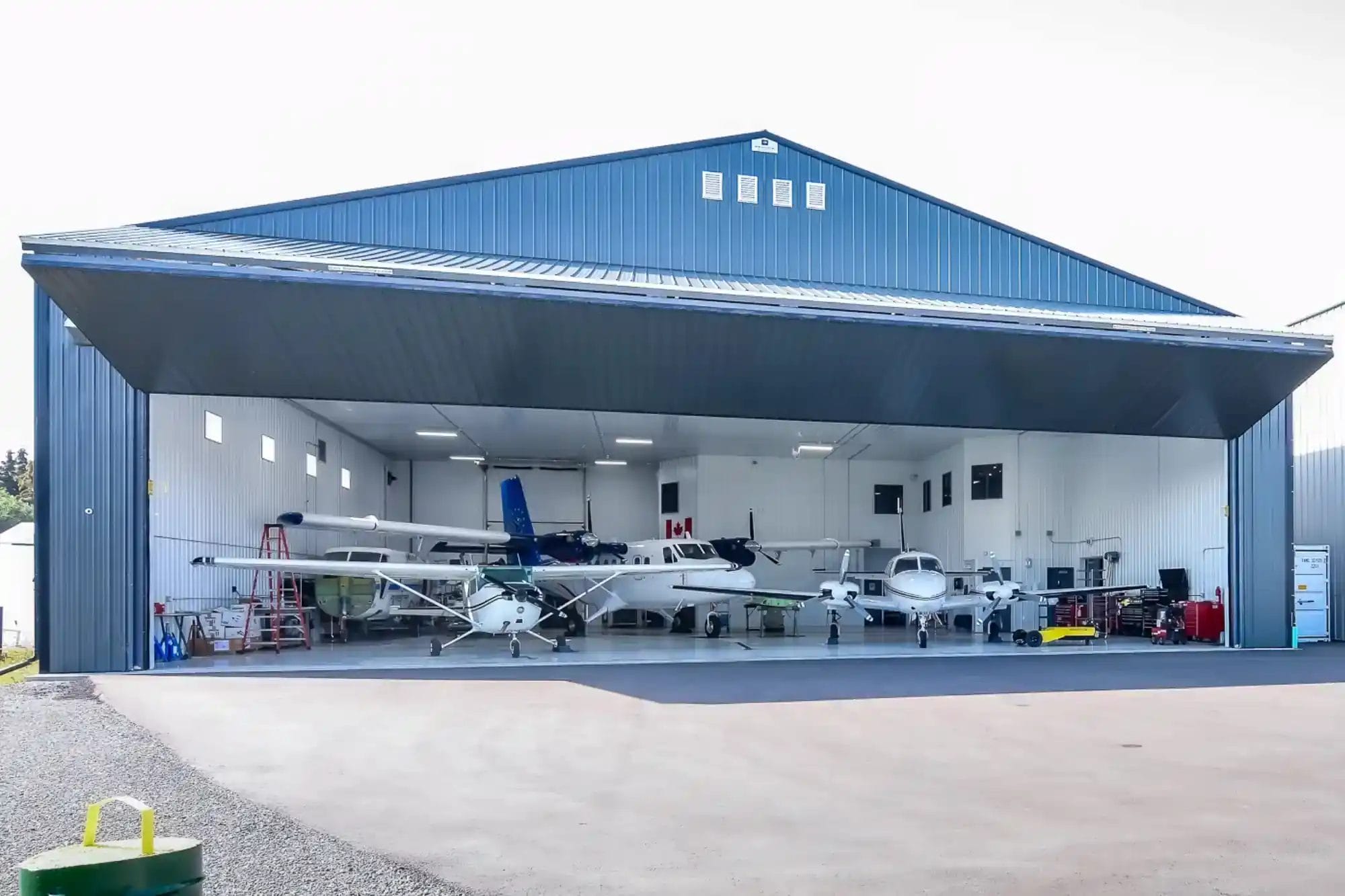 Post Frame Building Aircraft Hangar With The Bi-fold Door Open To Show A Fleet Of Small Airplanes