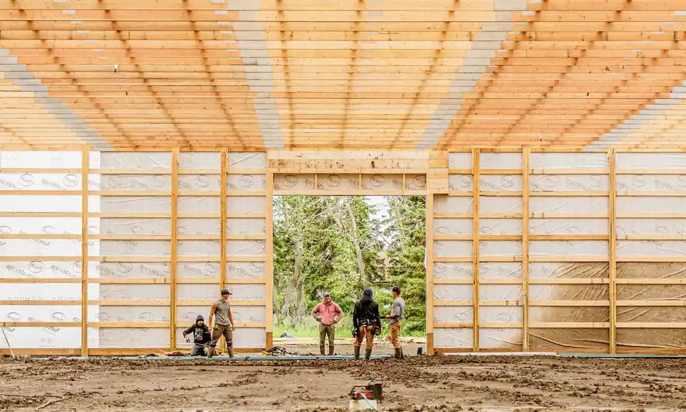Post frame construction process in action, with crew members cutting metal cladding
