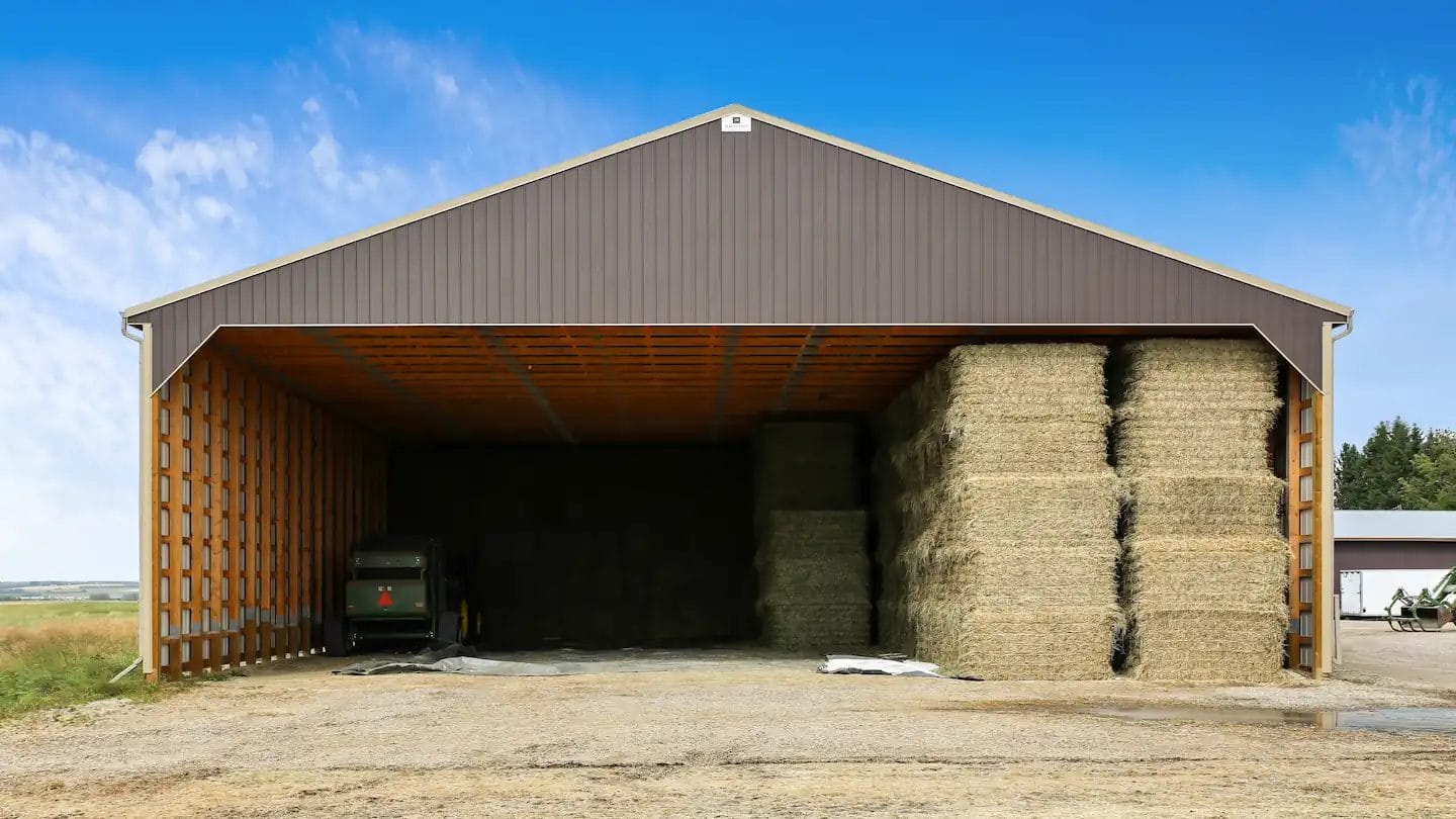 Hay bales stacked inside a large post frame hay barn