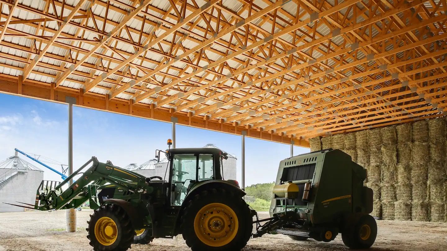 A John Deere tractor parked inside a large pole hay barn