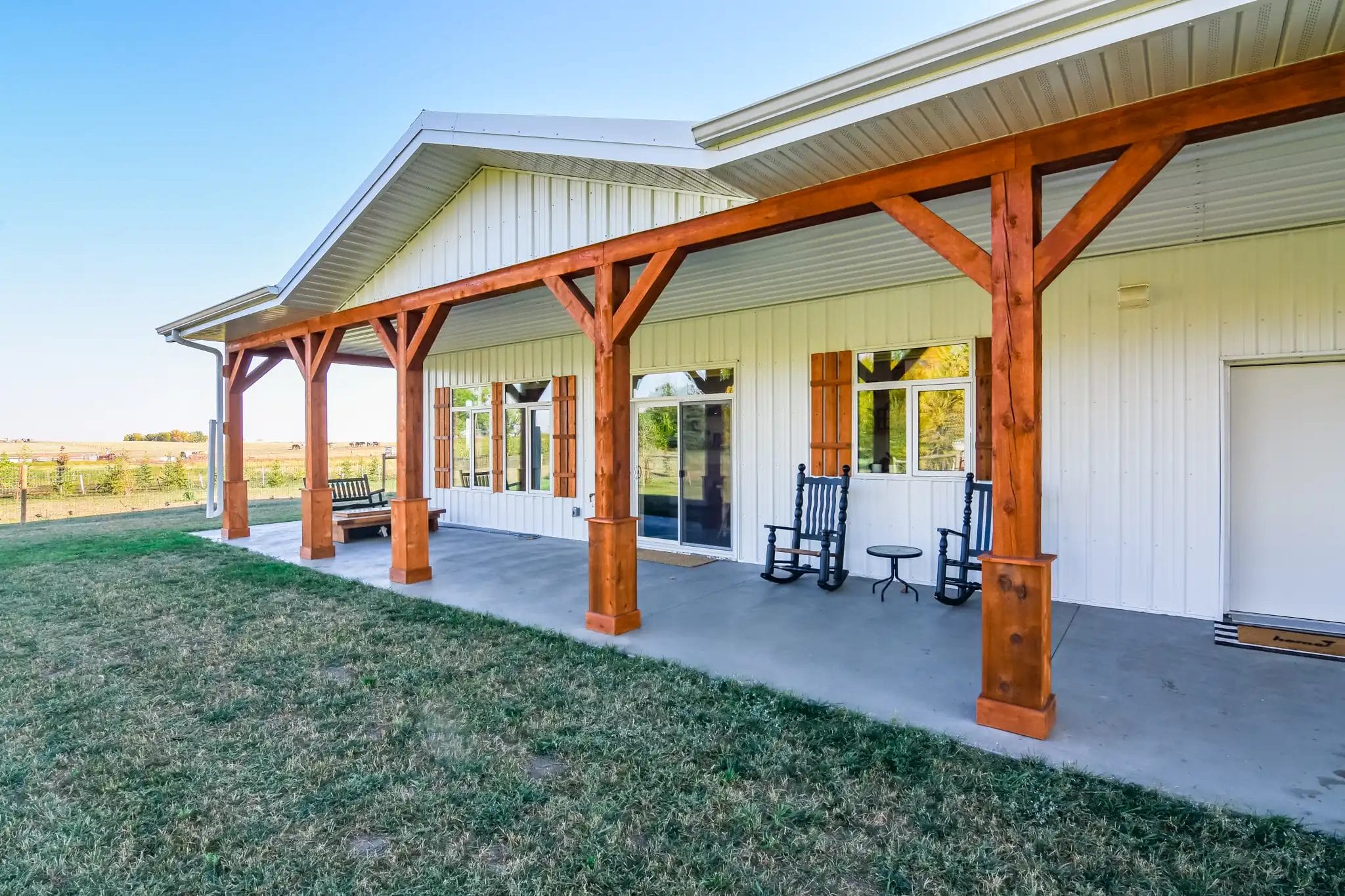 Covered porch on a white single story barndominium with exposed fir beams