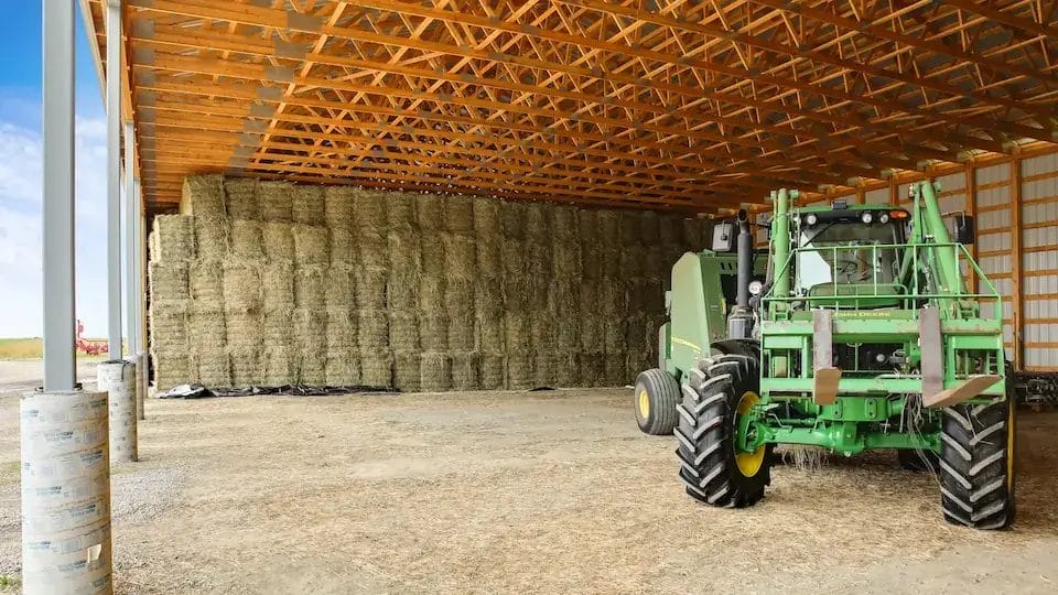 Hay storage shed building with farm equipment parked inside